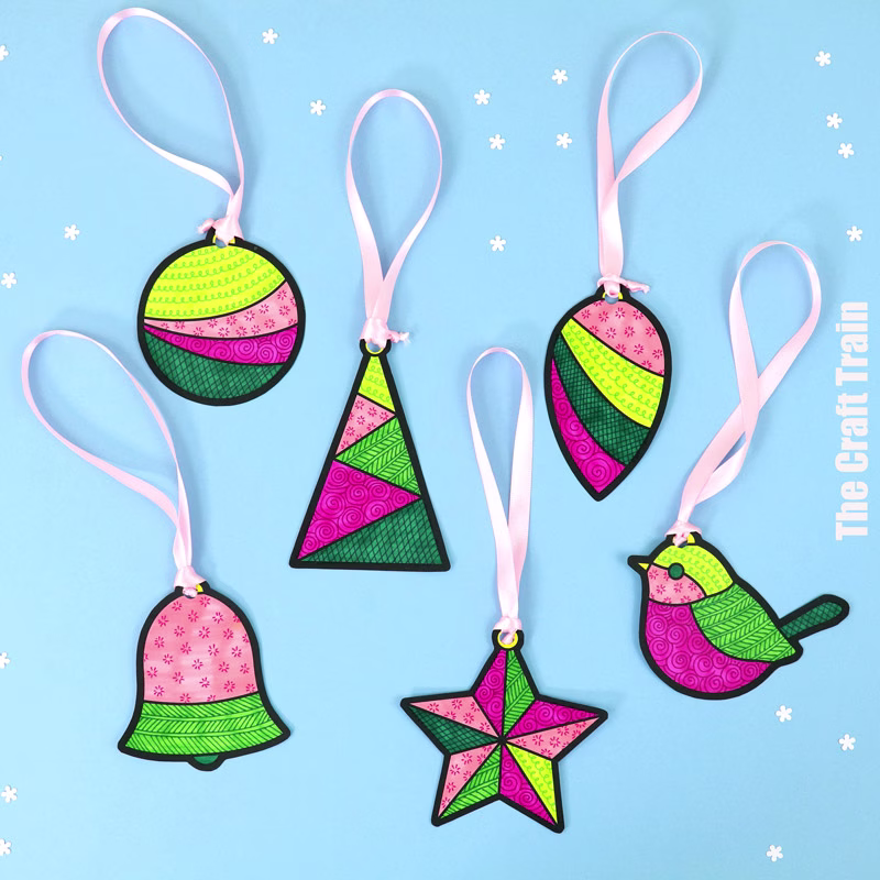Christmas pattern art decorations photographed on a pale blue background. The decorations include various Christmas shapes printed to paper, then coloured in and decorated with patterns. Pink ribbon has been threaded through the top of each decoration to hang them with.