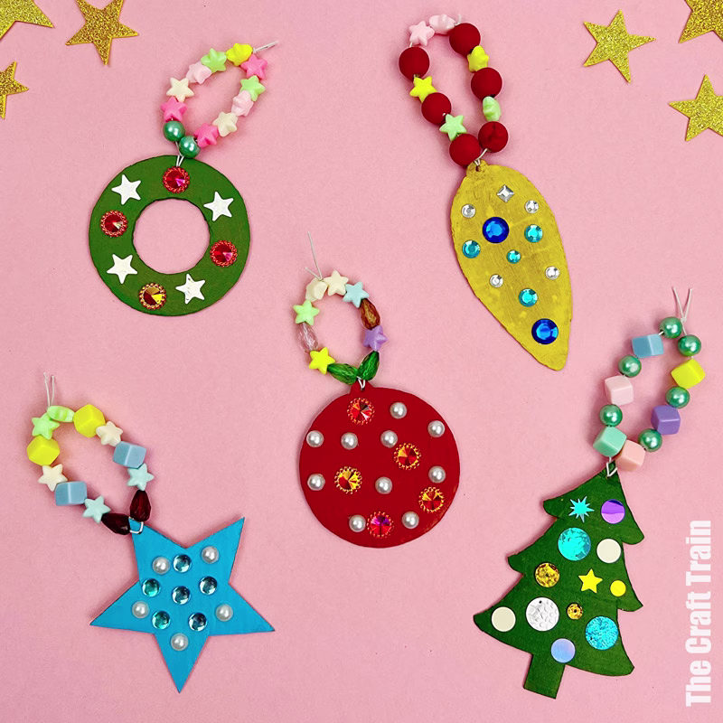 Recycle cardboard Christmas ornaments. There is a wreath, two baubles, a star and a tree decorated with plastic rhinestones and sequins, photographed on a pink background