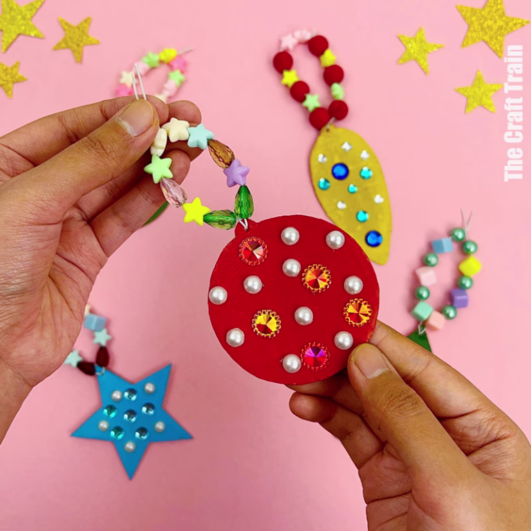 Recycle cardboard Christmas ornaments. A handmade red painted cardboard bauble shape with beaded string is being held, surrounded by other handmade Christmas shape ornaments.