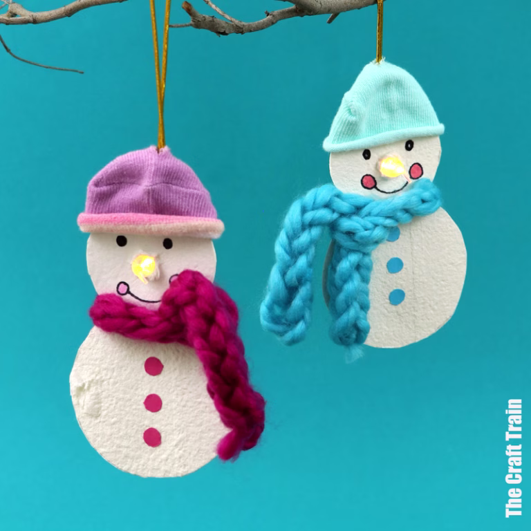 Egg carton snowman ornament suspended by a gold thread. The snowman is made from the lid of an egg carton with an LED candle for the nose